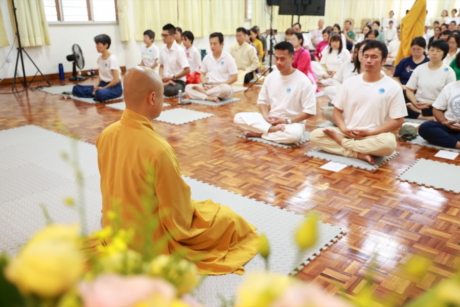 A monk guiding a hall of participants in seated meditation