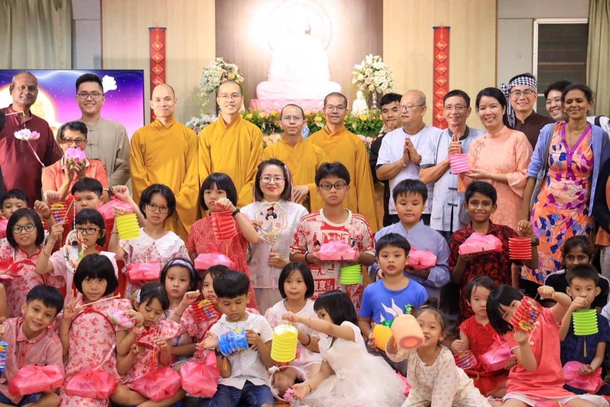 Monks and families with children holding lanterns in front of the Buddha altar